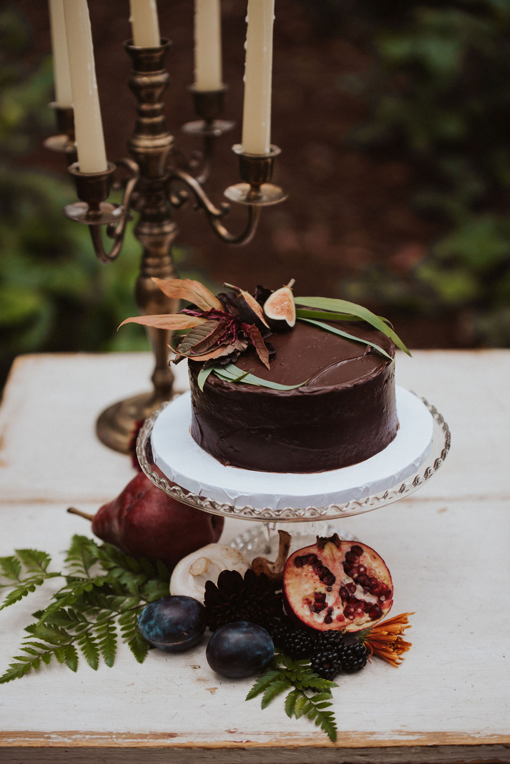 a chocolate wedding cake with floral decoration sitting on a white table in the forest