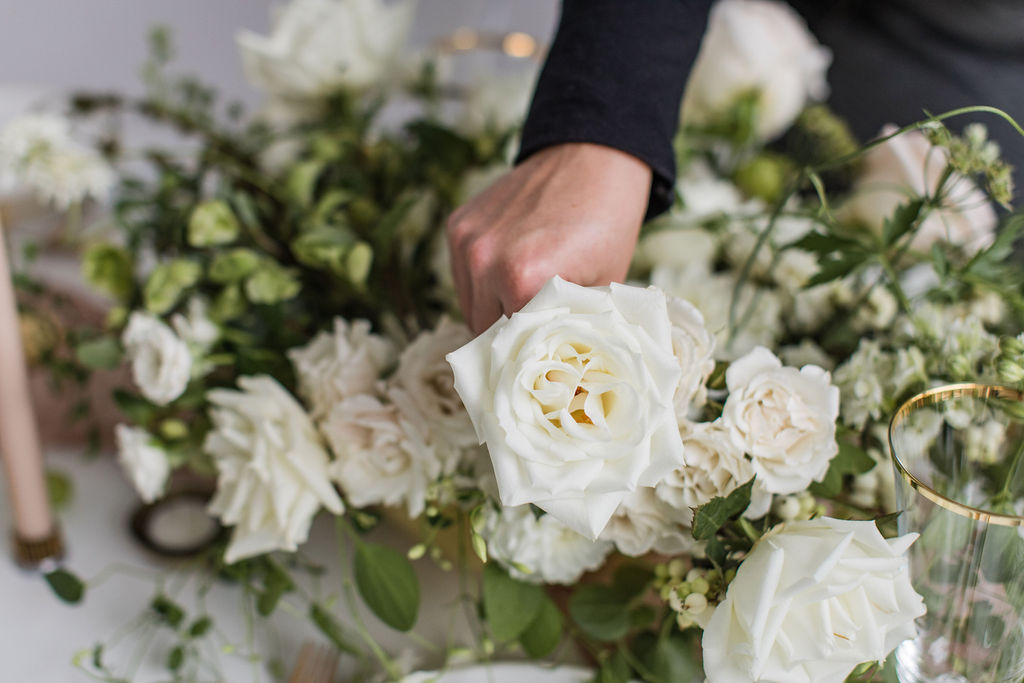 Folk Art Flowers owner Carolyn Kulb's hand places a white rose in a green and white centerpiece on a wedding table