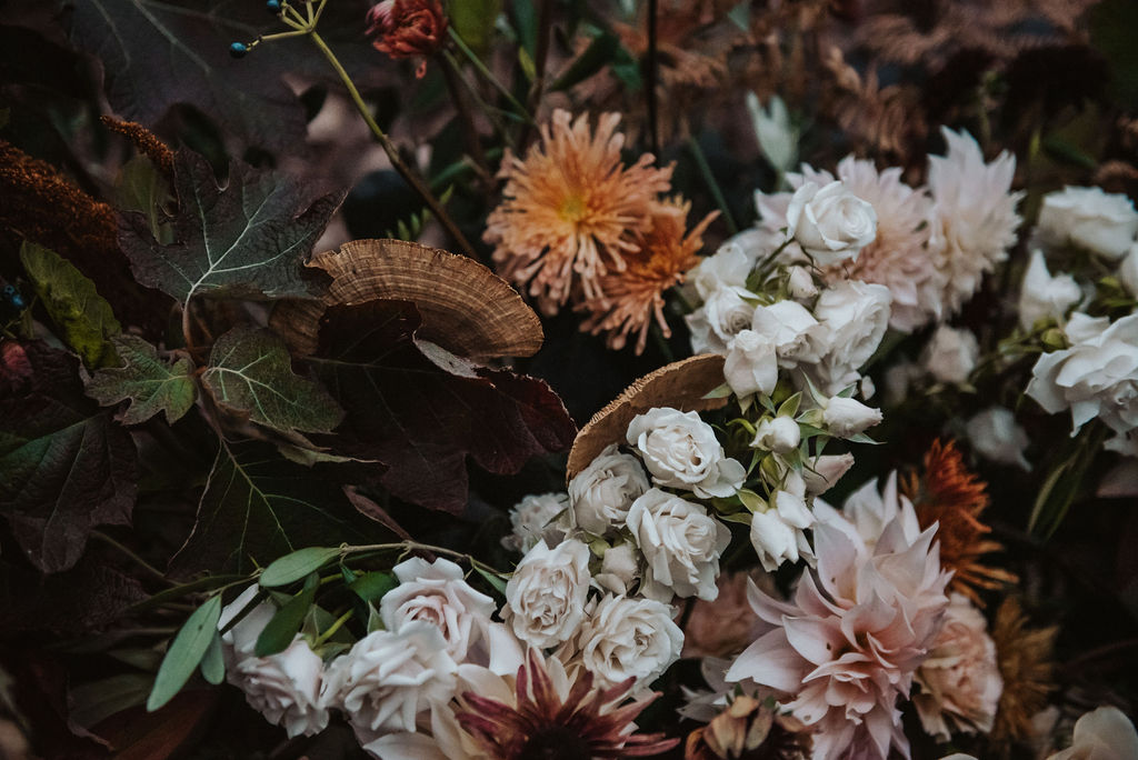 a grounded floral arch with fall foliage, mushrooms, spray roses, and heirloom mums